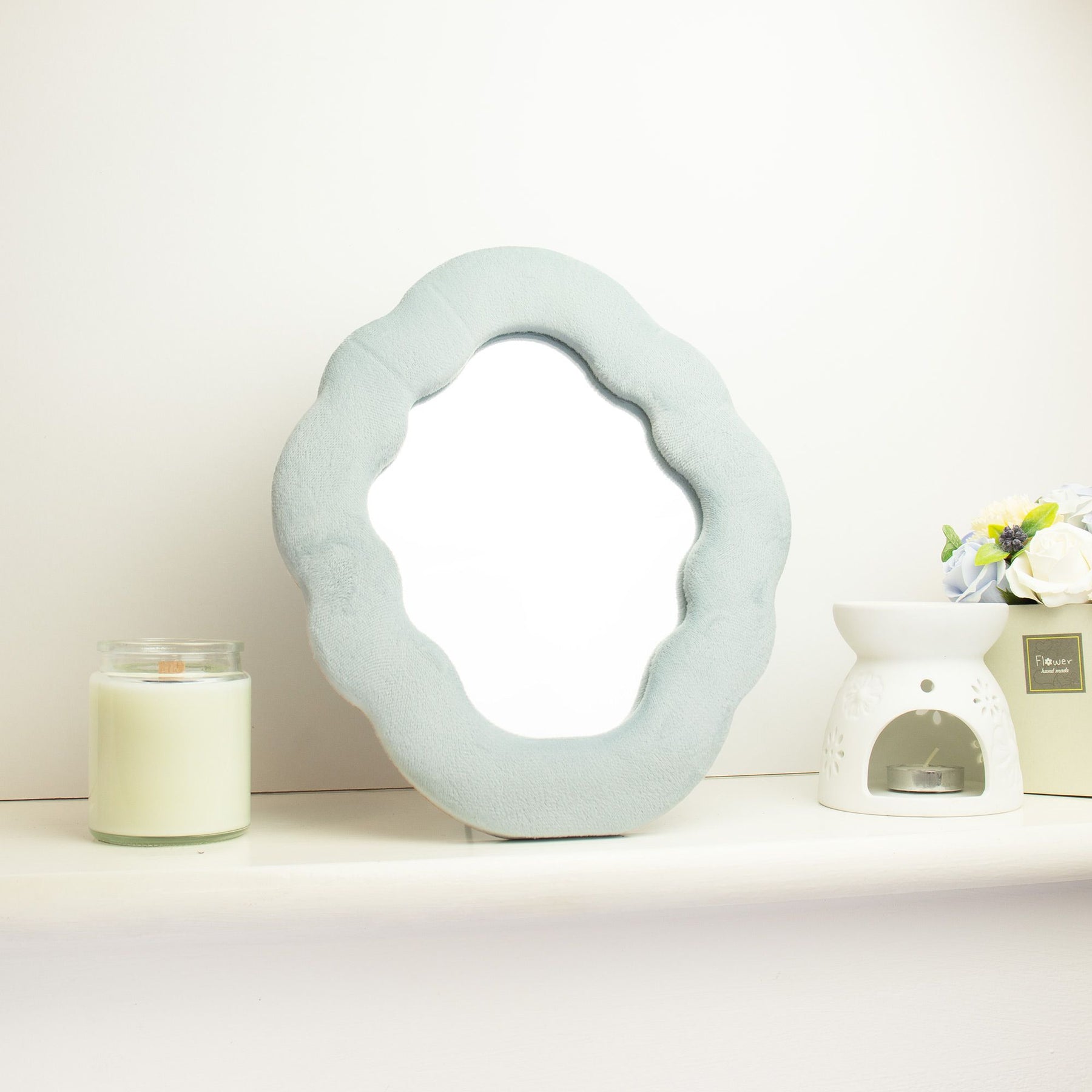 Soft squiggly cloud mirror in serene Cloud Blue velvet frame with smooth rounded silhouette, freestanding on white dressing table with soft natural light reflecting in glass