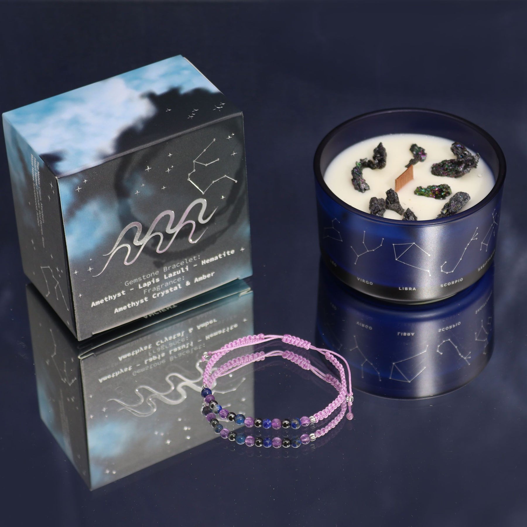 Candle with decorative elements, packaging, and bracelet on a reflective surface