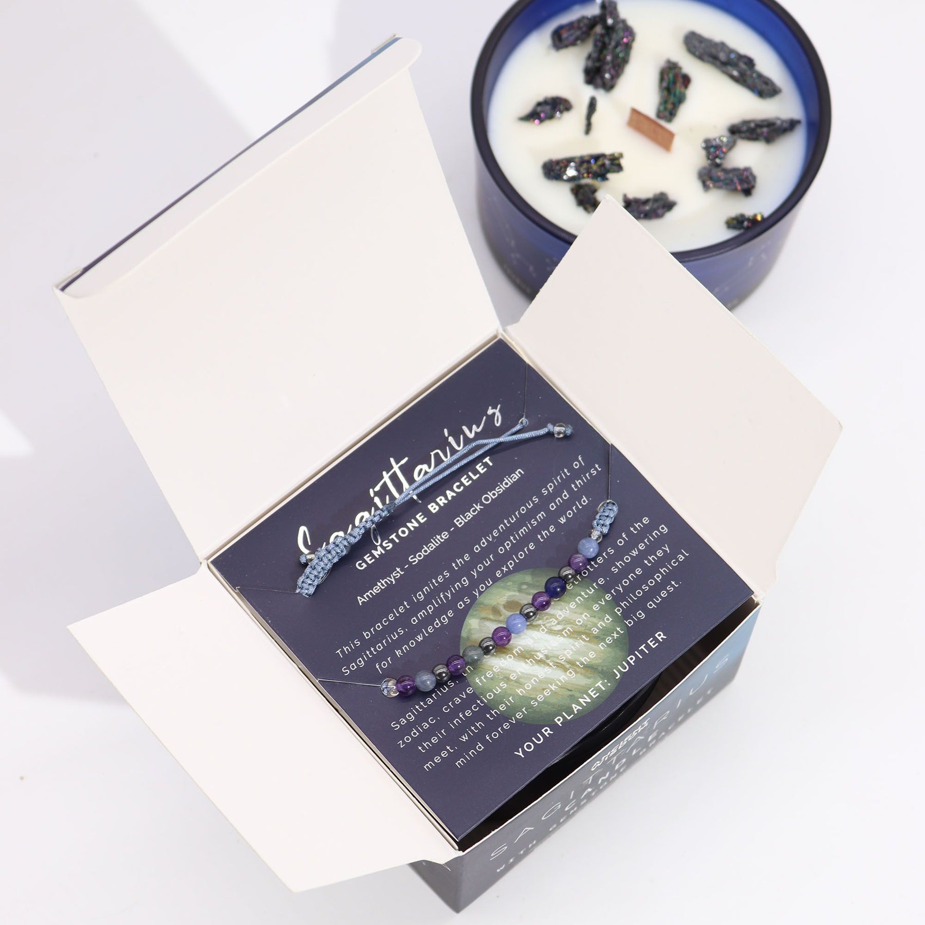 Box of gemstone bracelets with a candle featuring crystals on a white background