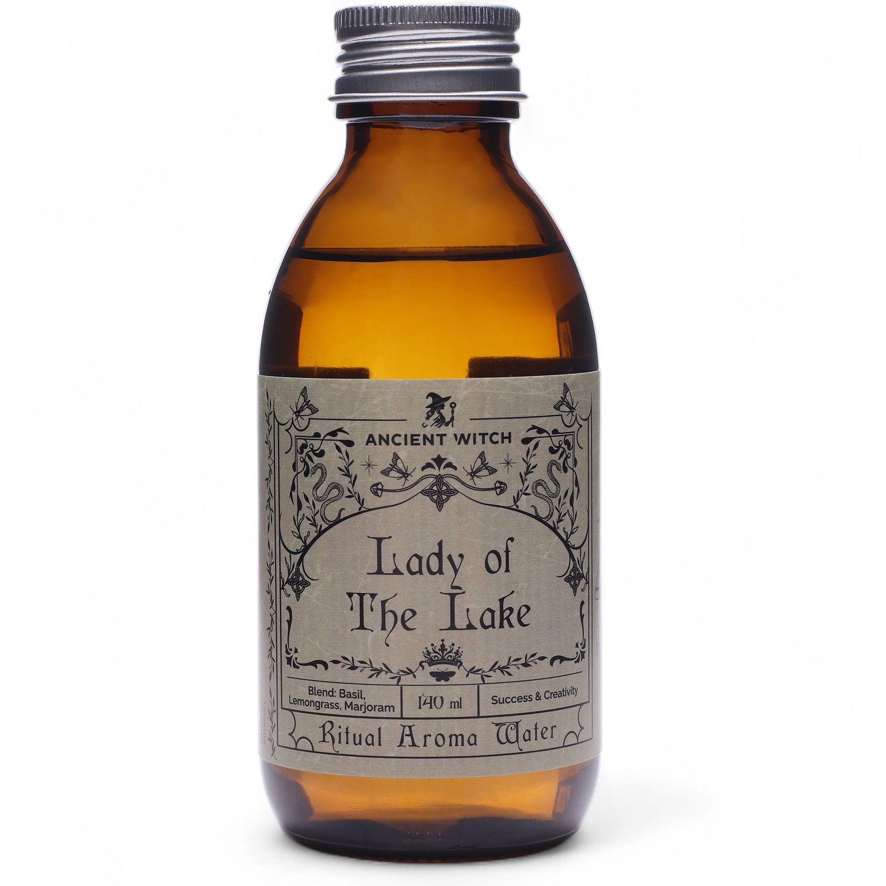 140ml amber glass bottle of Lady of the Lake ritual water with sword-in-lake label, surrounded by fresh basil, lemongrass, misty water and Excalibur sword