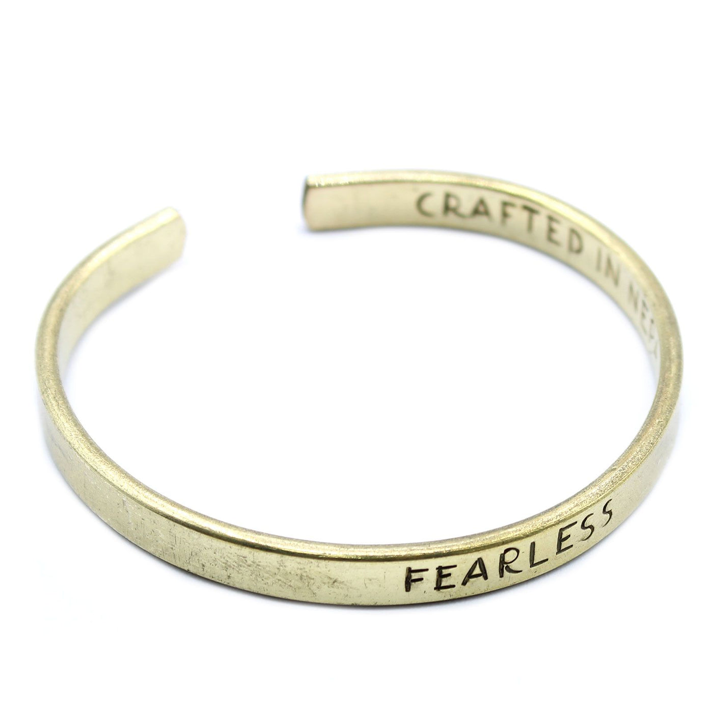 Golden brass mantra cuff engraved “FEARLESS” on wrist, Himalayan prayer flags and snow-capped peaks in soft background light