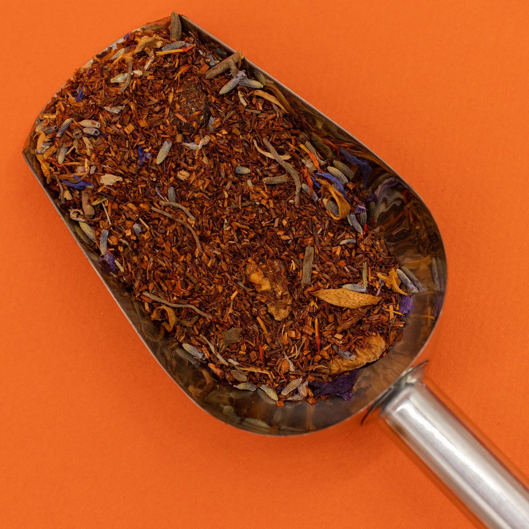 Metal scoop filled with dried herbs against an orange background