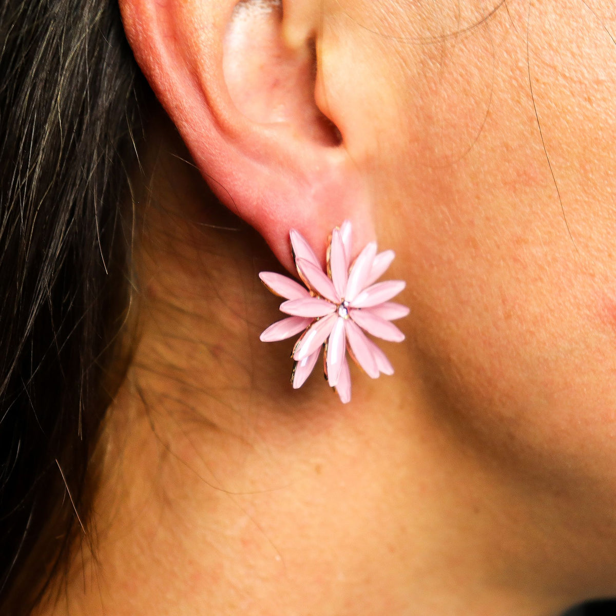 Close-up of a pink flower-shaped earring worn by a person.