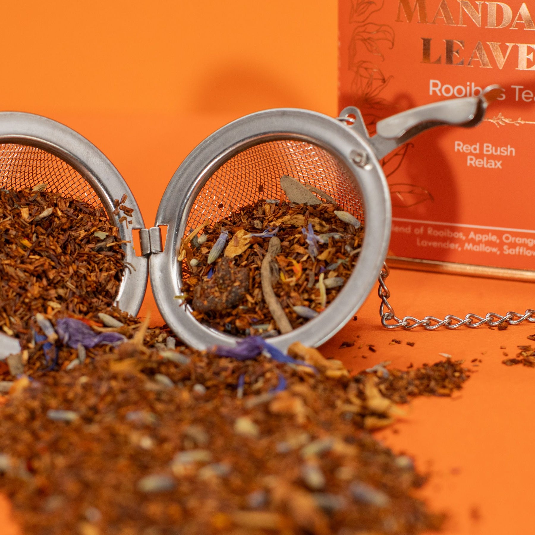 Tea leaves in a metal mesh tea ball with an orange background and tea box.