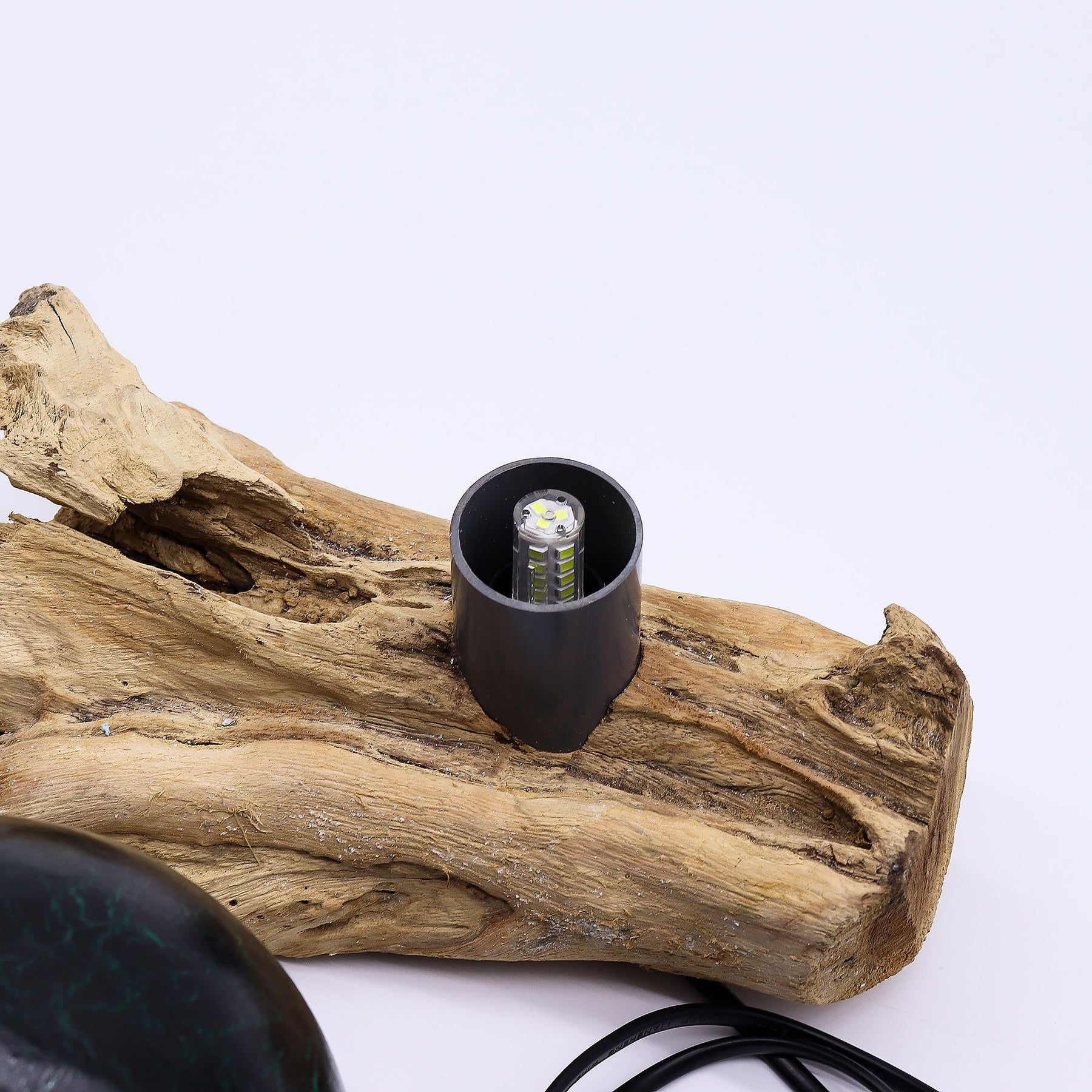 Emerald crackle glass sphere glowing atop unique twisted driftwood base on dark wooden side table with books and plants at night