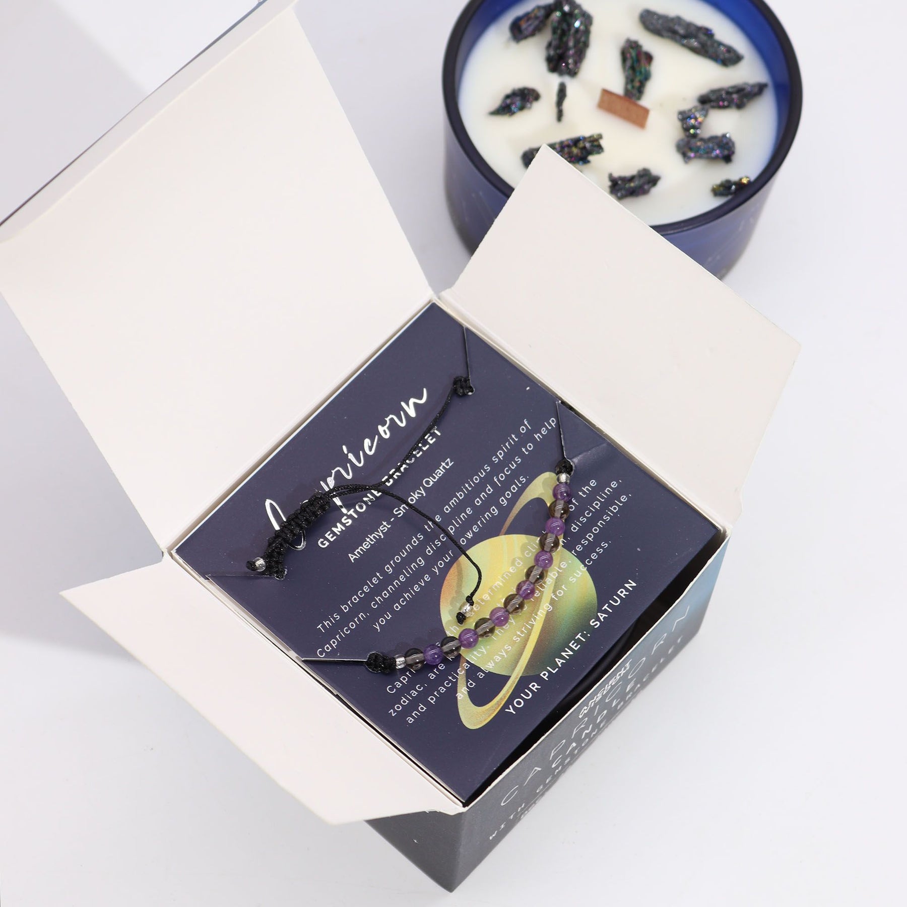 Navy & gold Capricorn zodiac candle burning beside matching amethyst & smoky quartz bracelet, styled with Capricorn constellation card and mountain crystals