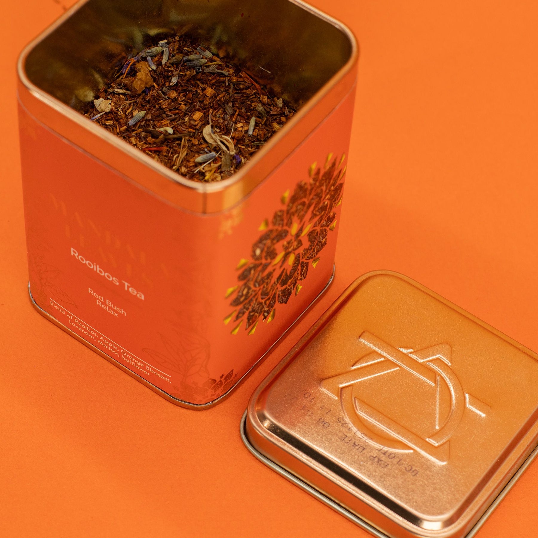 Open orange tea tin with mandala leaves branding on an orange background