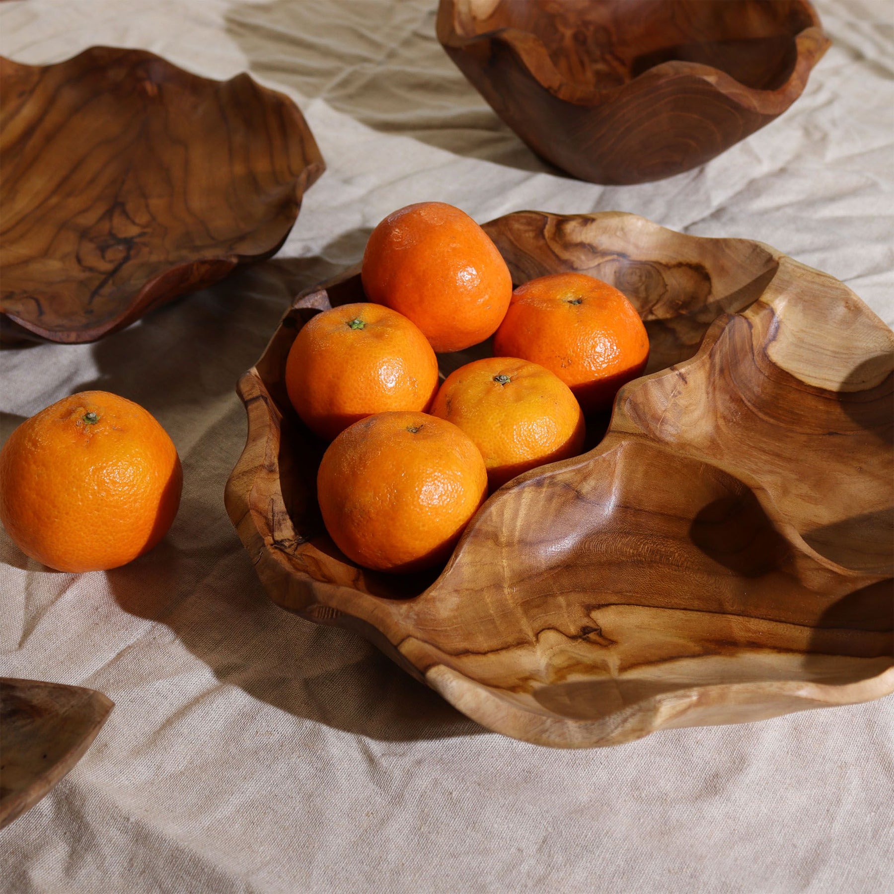 Smooth round teakwood fruit bowl with three divided sections, rich natural grain visible, filled with fresh fruit, nuts and snacks on a dining table in bright kitchen setting