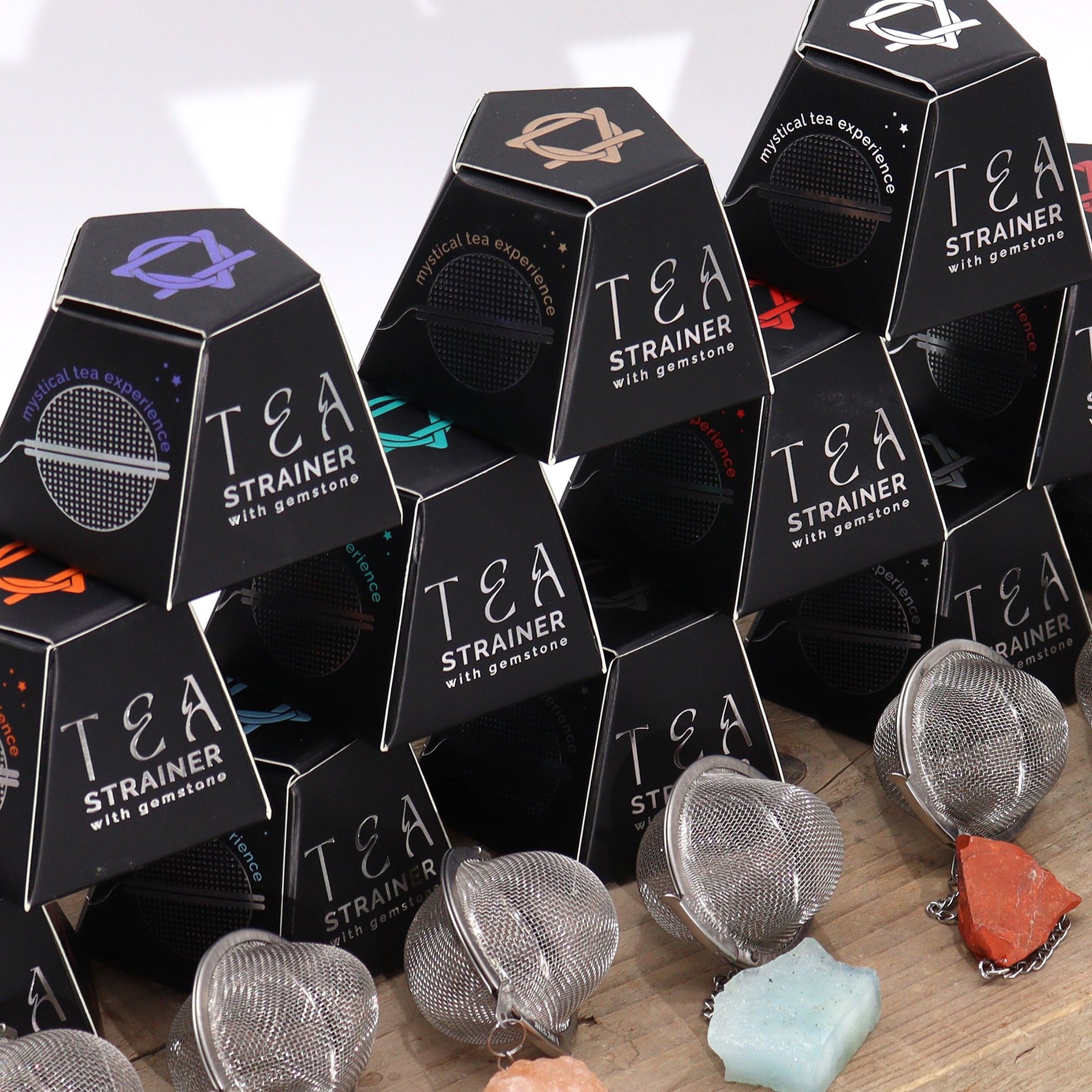 Tea strainers with gemstones in black hexagonal packaging on a wooden surface.