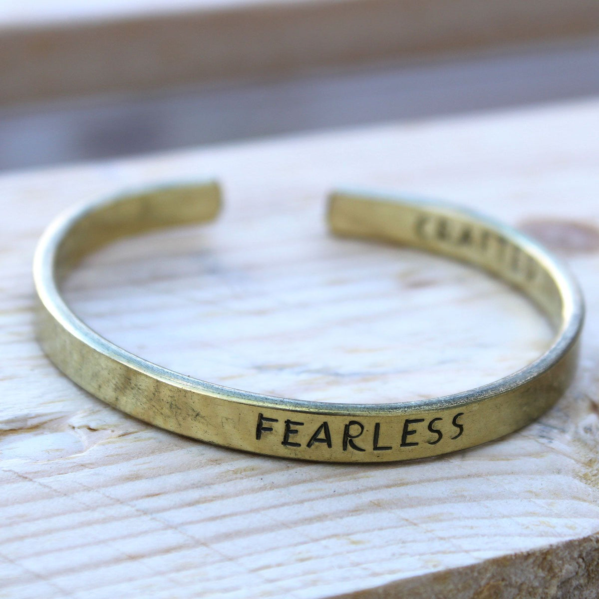 Gold bracelet with 'FEARLESS' engraved on a light wooden surface
