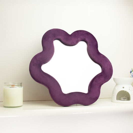 Soft squiggly star mirror in muted mauve velvet frame with gentle wavy edges, freestanding on white shelf with soft natural light reflecting in glass