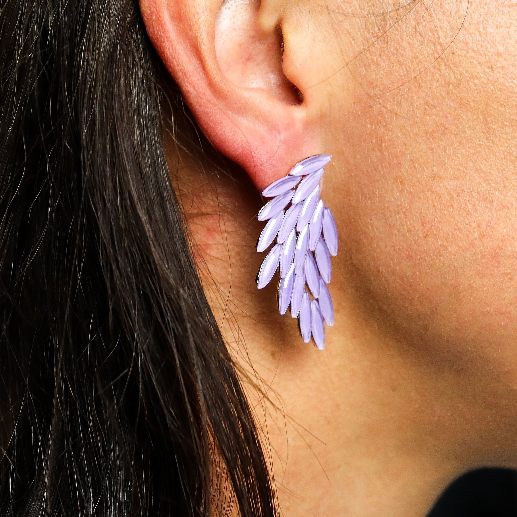Close-up of an ear wearing a purple feather-shaped earring