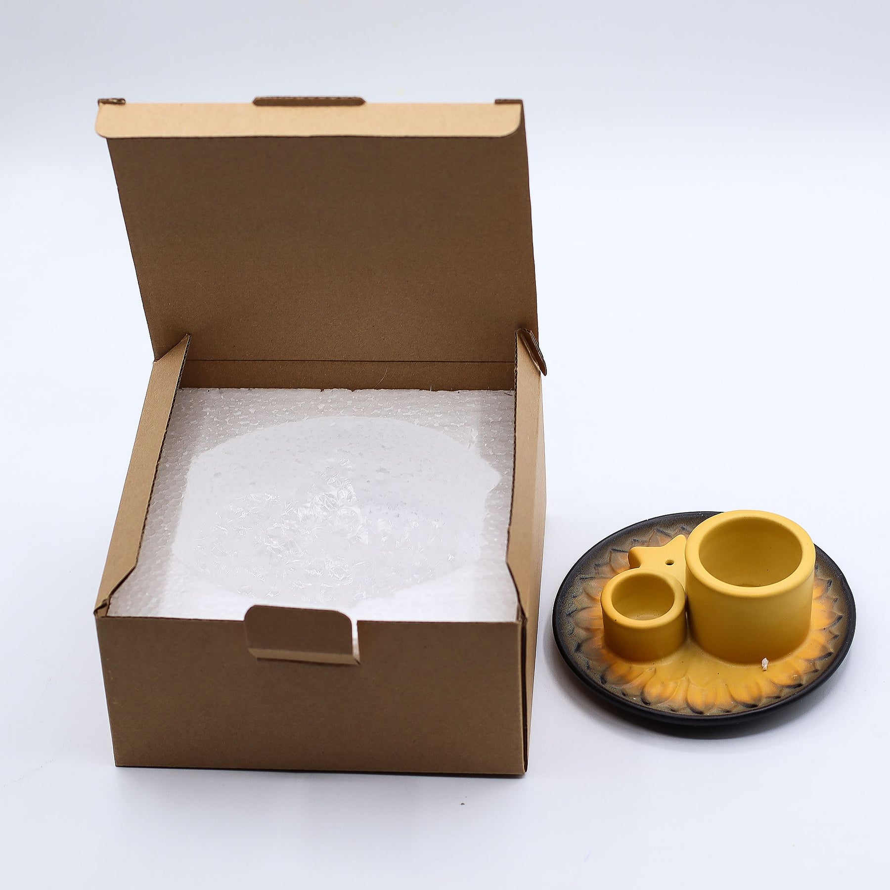 Open cardboard box with bubble wrap next to a set of yellow ceramic incense holder