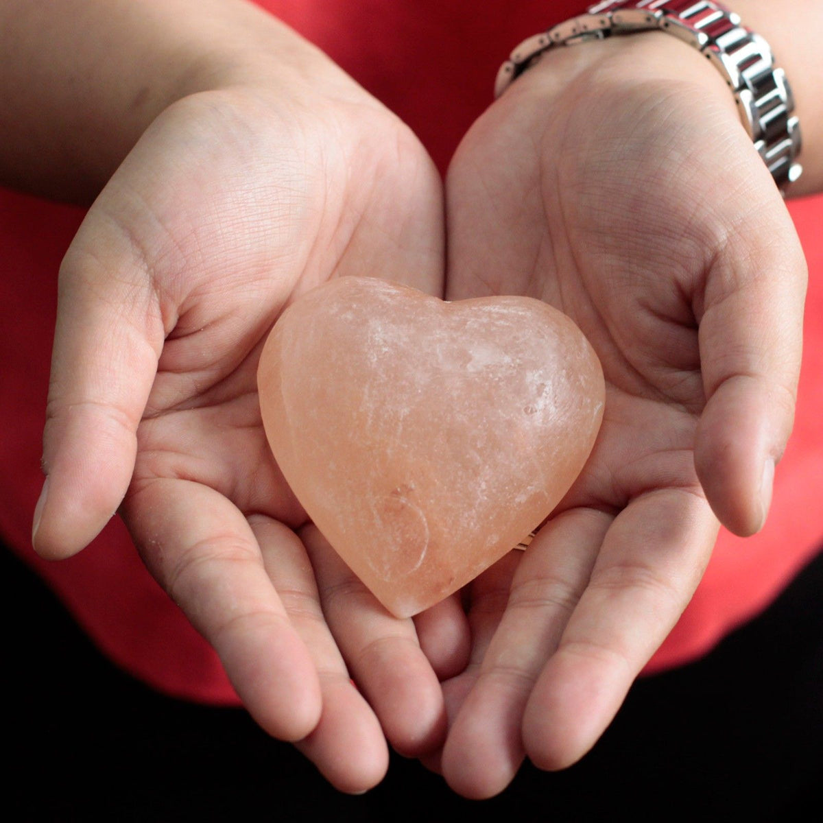 Heart-shaped himalayan heart deodorant stone held in hands against a red background