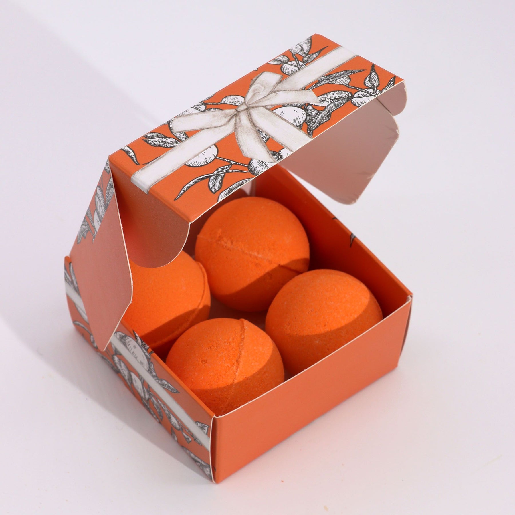 Orange bath bombs in a decorative box with floral design on a white background