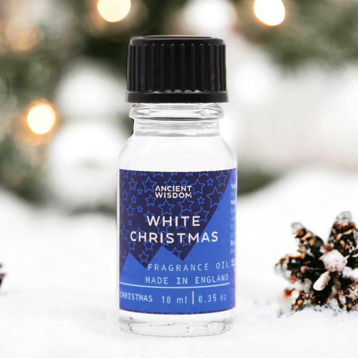 10ml White Christmas fragrance oil bottle surrounded by frosted pine, snowflakes and glittering snow on dark winter background