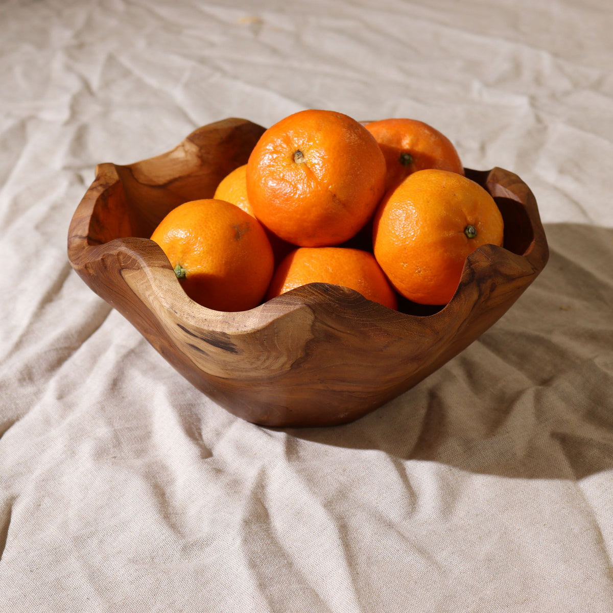 Medium smooth teakwood fruit bowl (21×9cm) with rich natural grain, filled with fresh fruit on a dinning table in bright kitchen setting