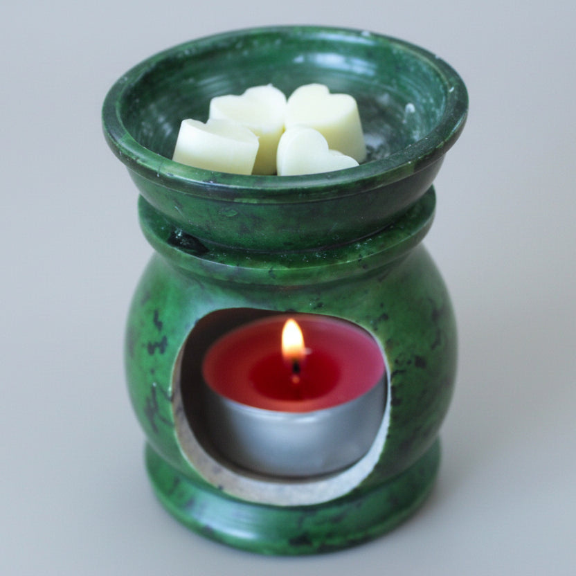 Green ceramic oil burner with wax cubes and a candle on a beige background