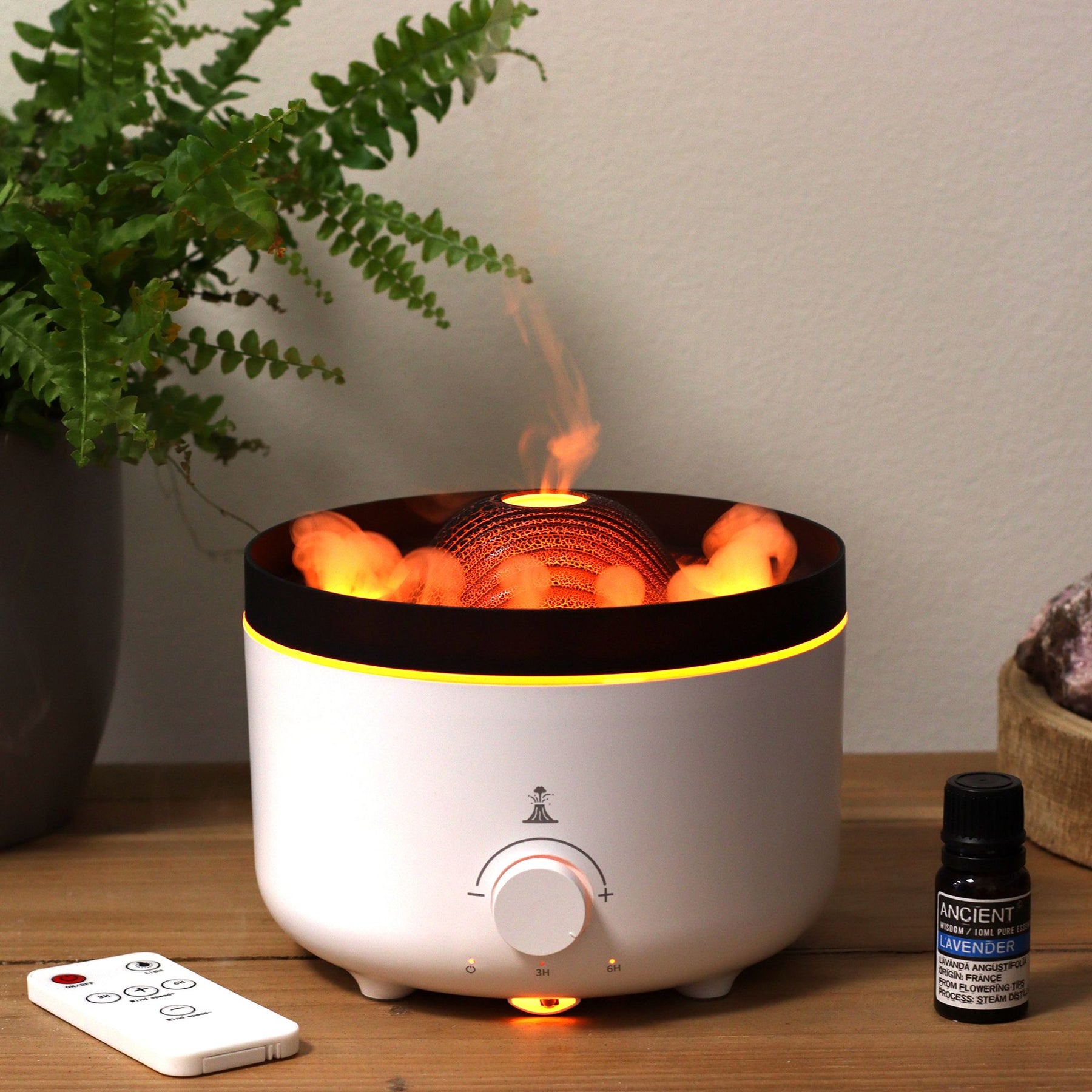 Large black volcano aroma diffuser erupting with swirling coloured mist and glowing LED ring, essential oil bottle beside