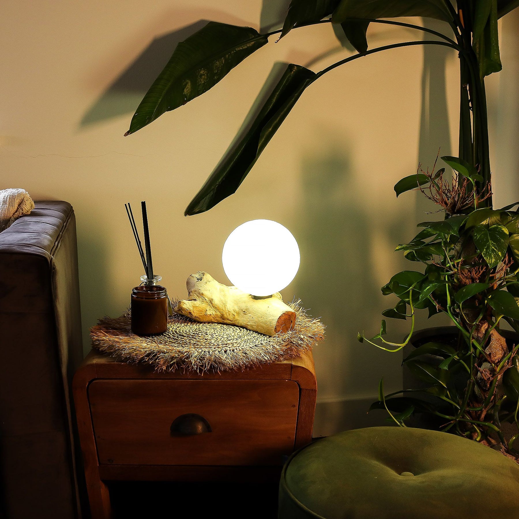 Glowing spherical lamp on a wooden side table with plants and a couch