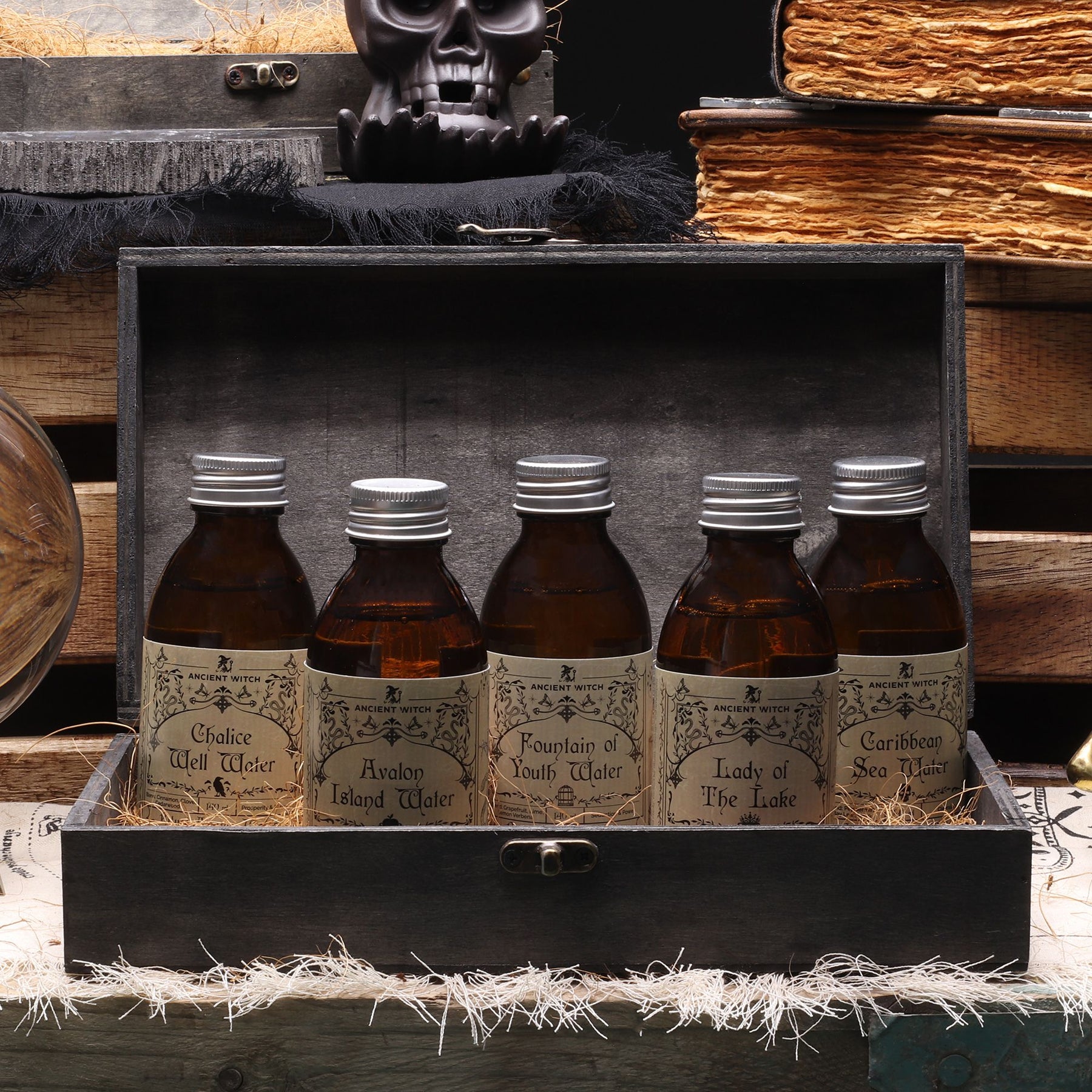 Five bottles of 'Water' in a wooden box with a skull and books in the background.