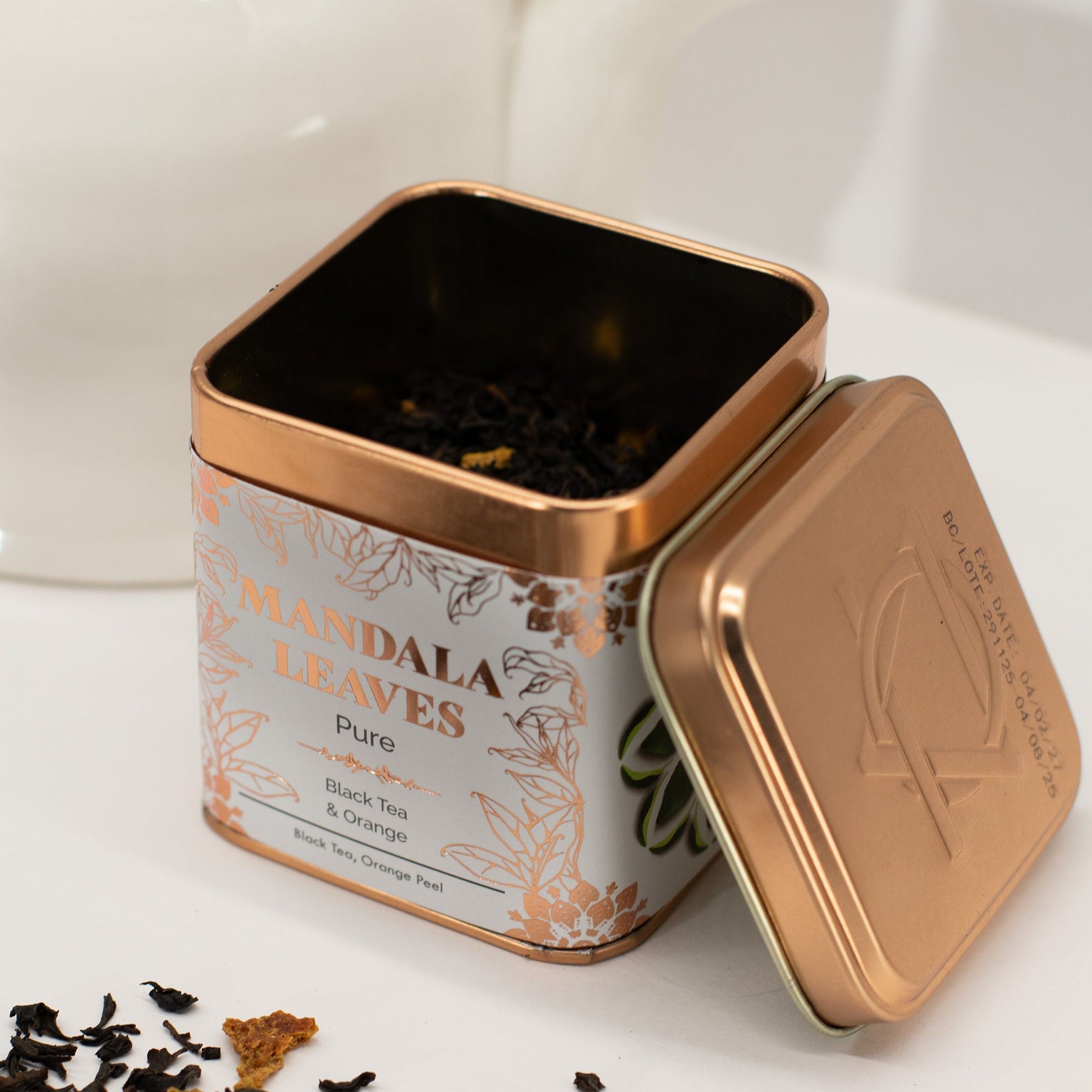 Tea canister labeled 'Mandala Leaves' with tea leaves spilling out on a white background