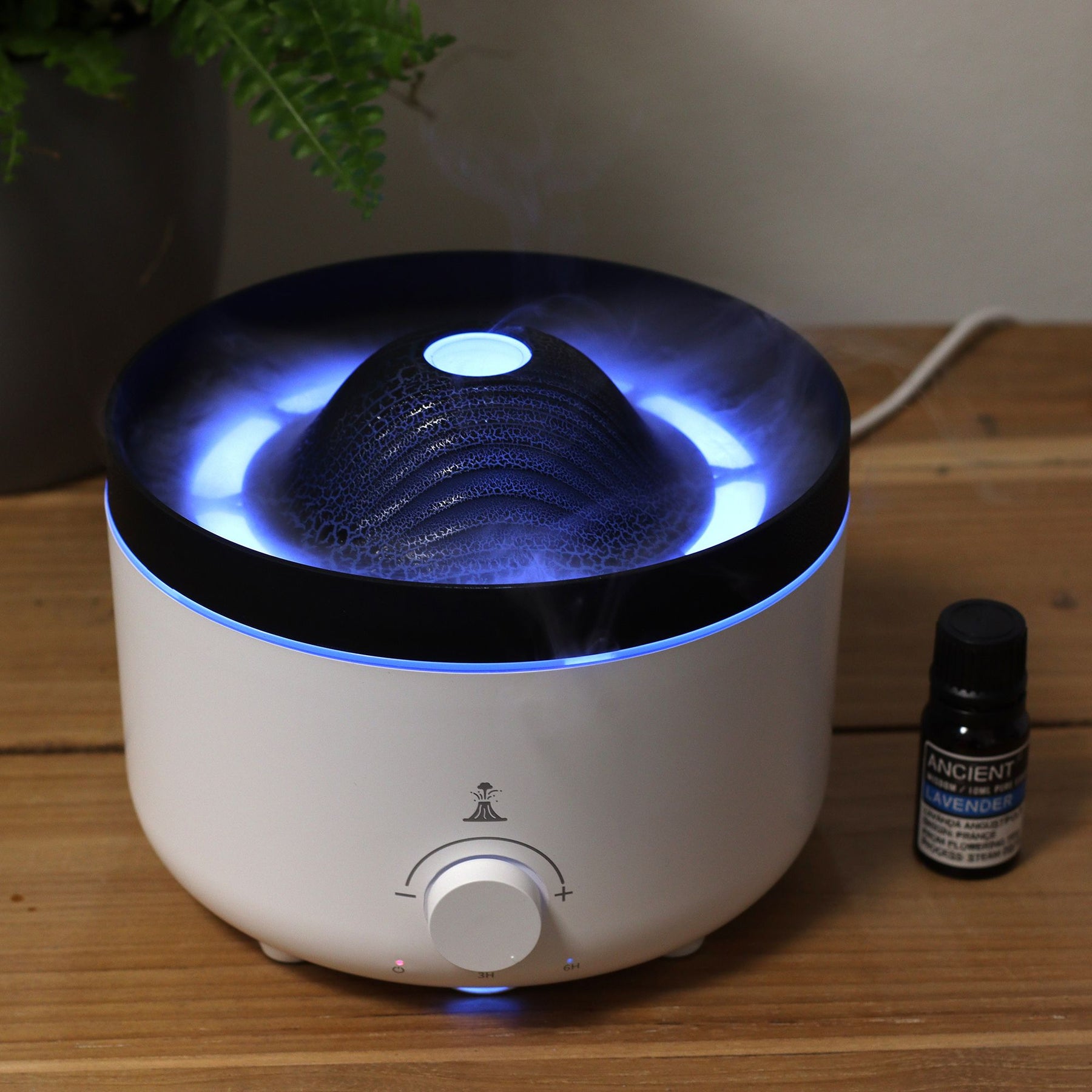Large black volcano aroma diffuser erupting with swirling coloured mist and glowing LED ring, essential oil bottle beside