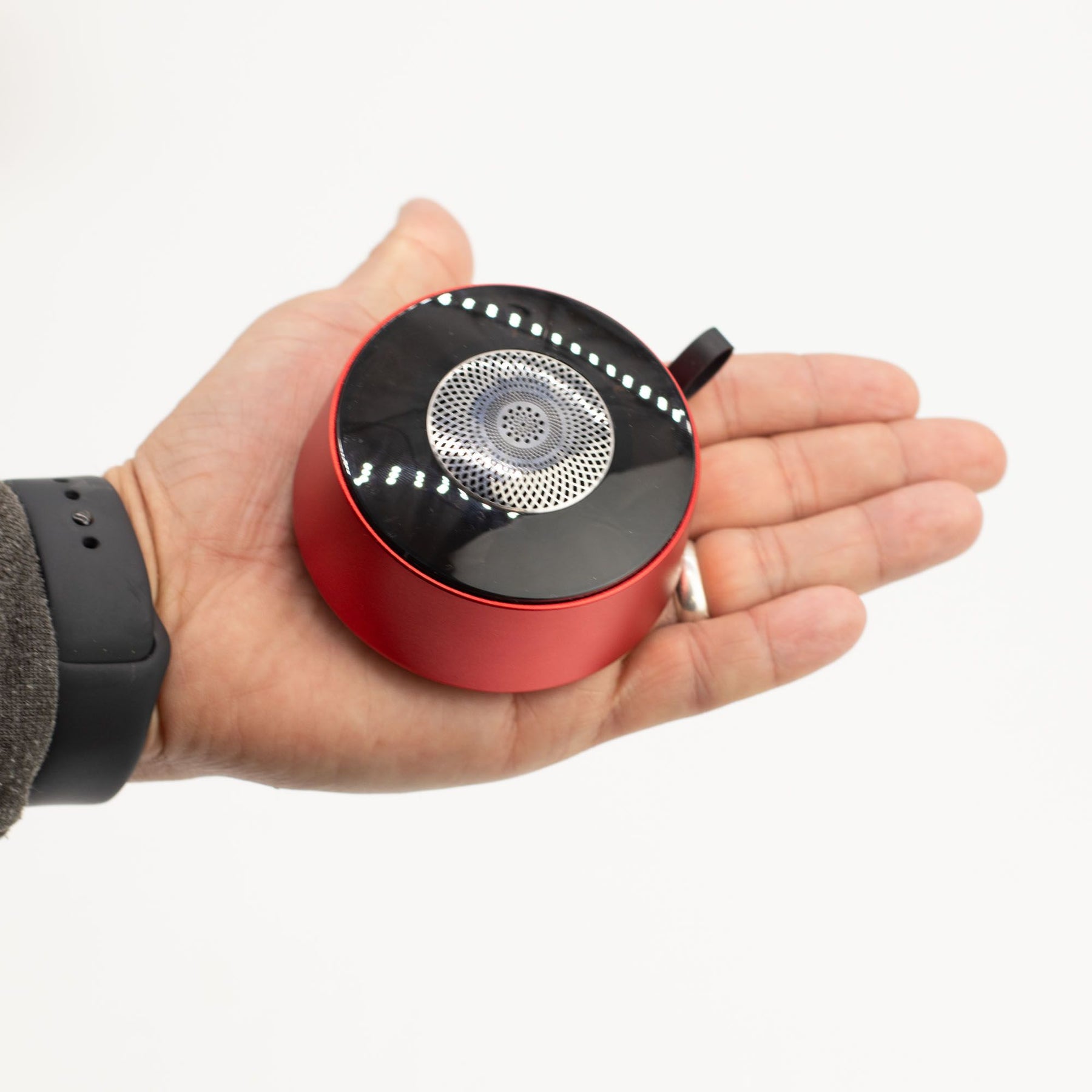 Speaker in hand demonstrating pocket-sized portability and integrated carry loop for easy transport