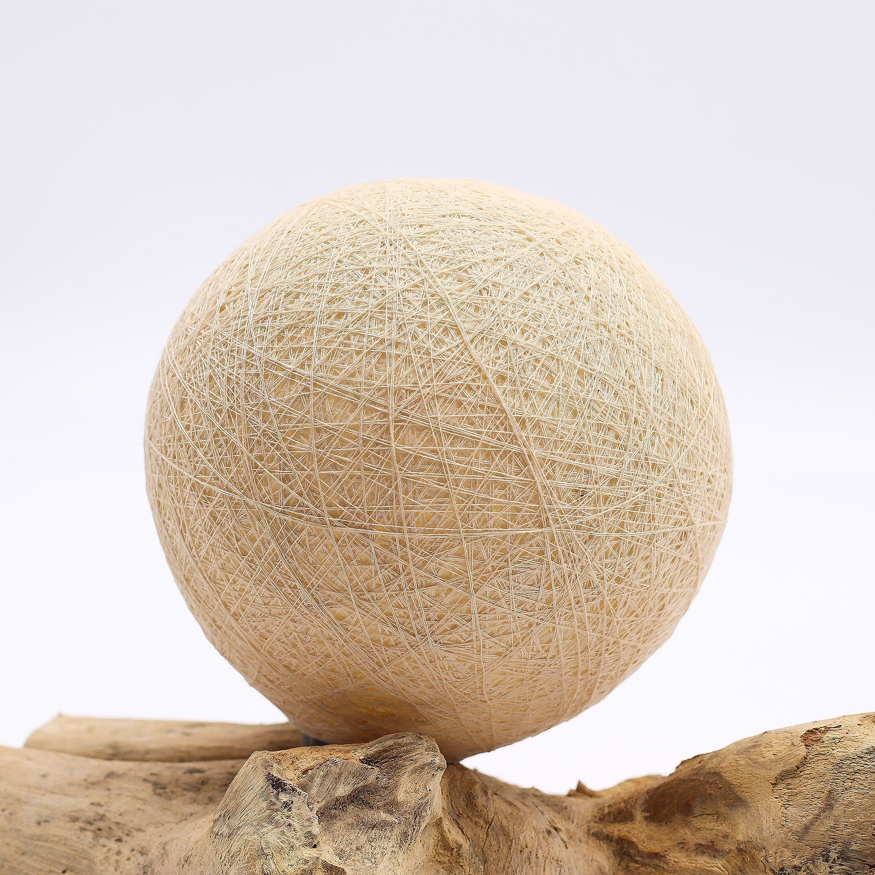 Cream cotton-wrapped sphere glowing gently atop twisted driftwood base
