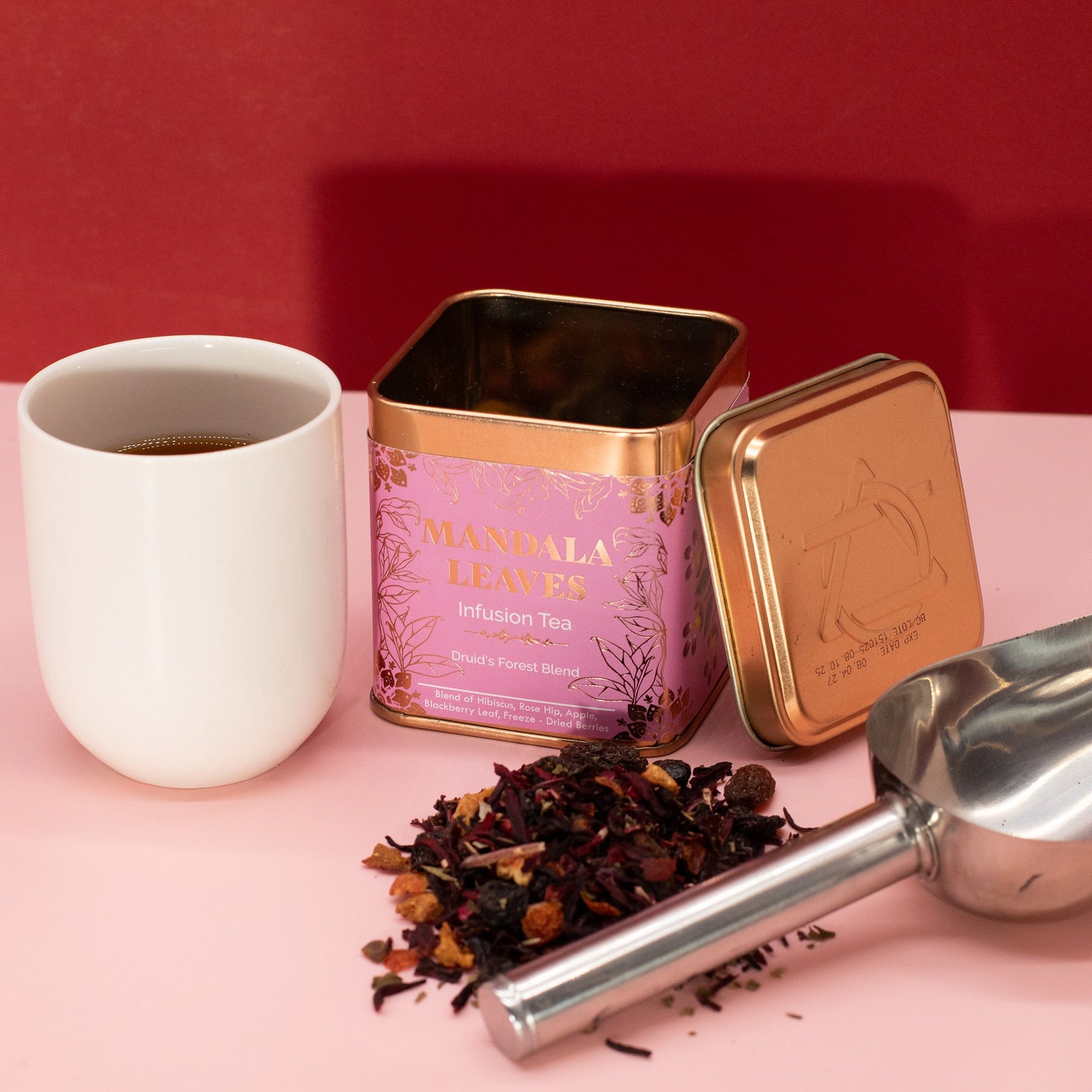 Tea canister with a scoop of tea leaves and a white cup on a pink surface with a red background