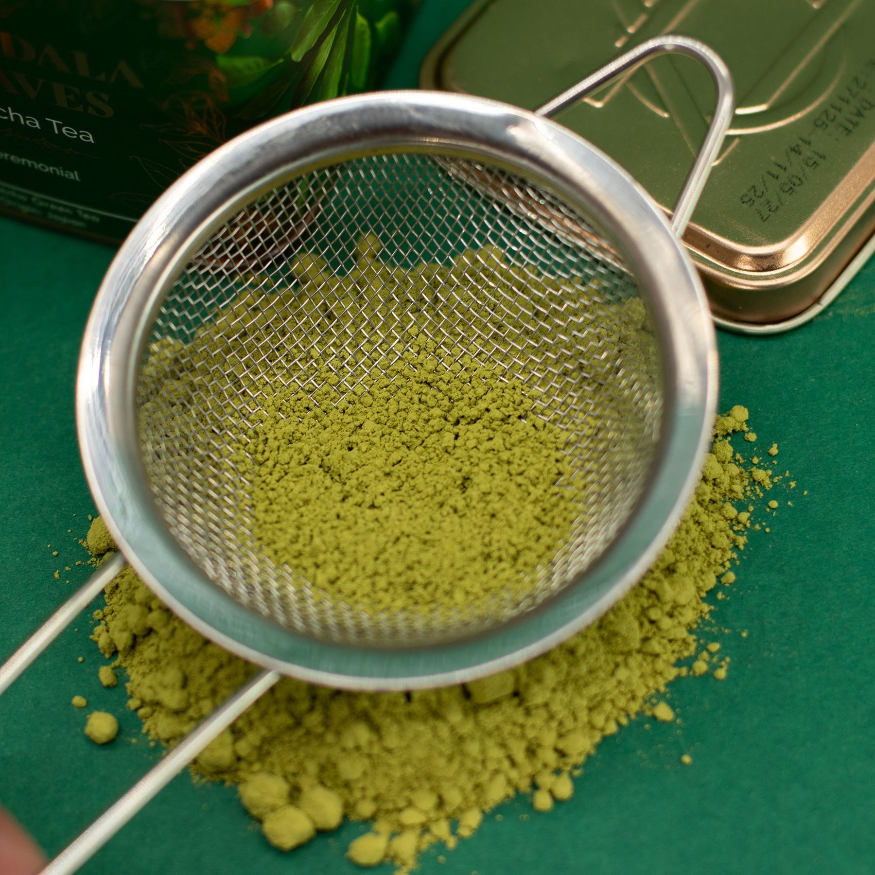 Matcha green tea powder in a metal mesh strainer on a green surface