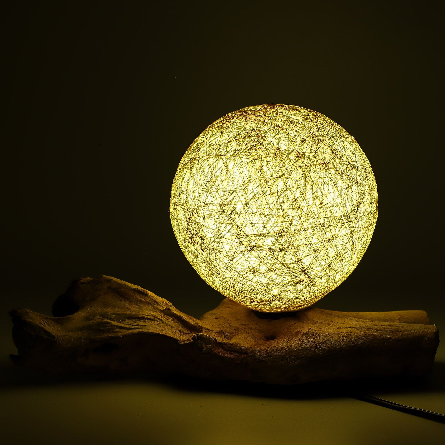 Cream cotton-wrapped sphere glowing gently atop twisted driftwood base
