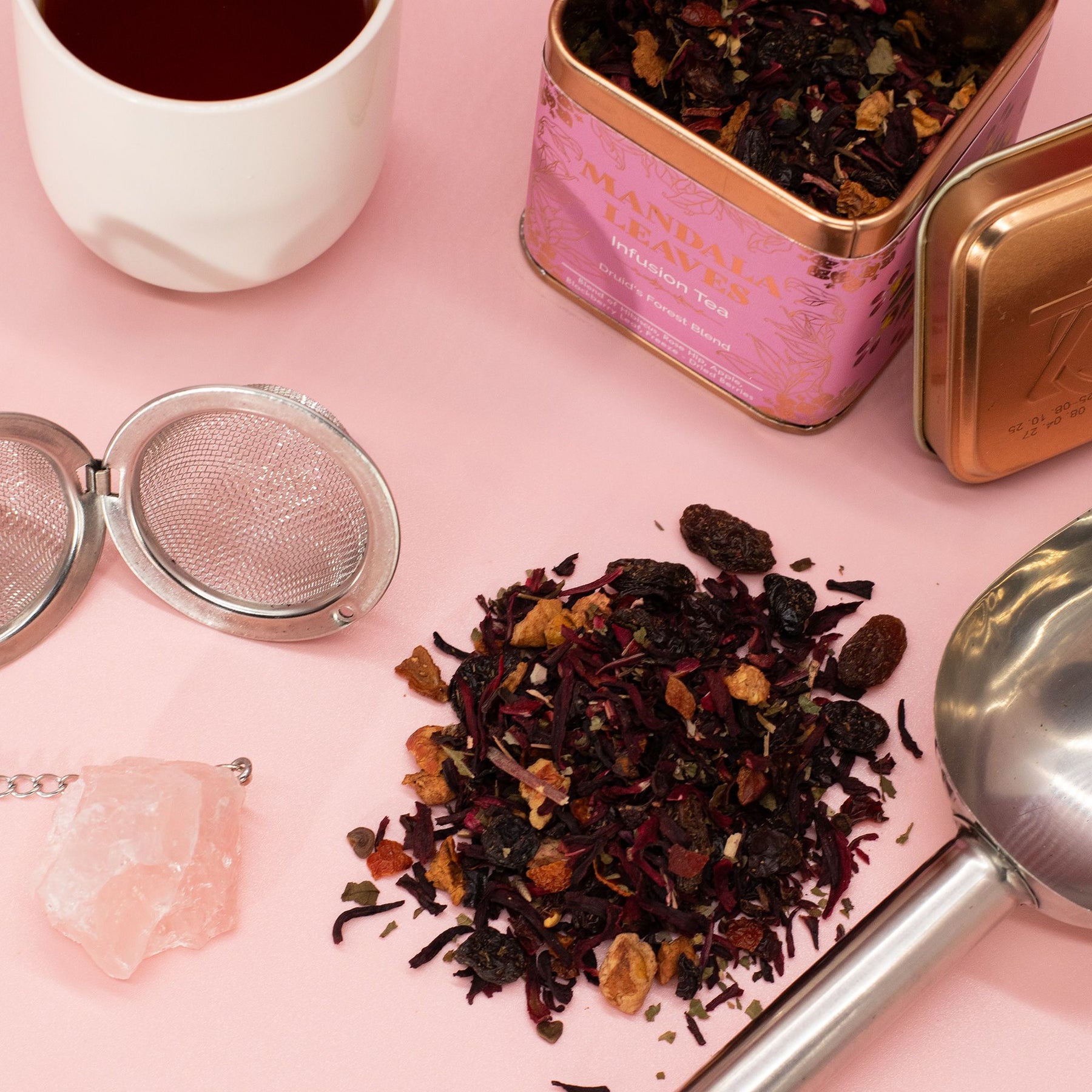 Tea leaves, tea strainer, and pink tea canister on a pink surface