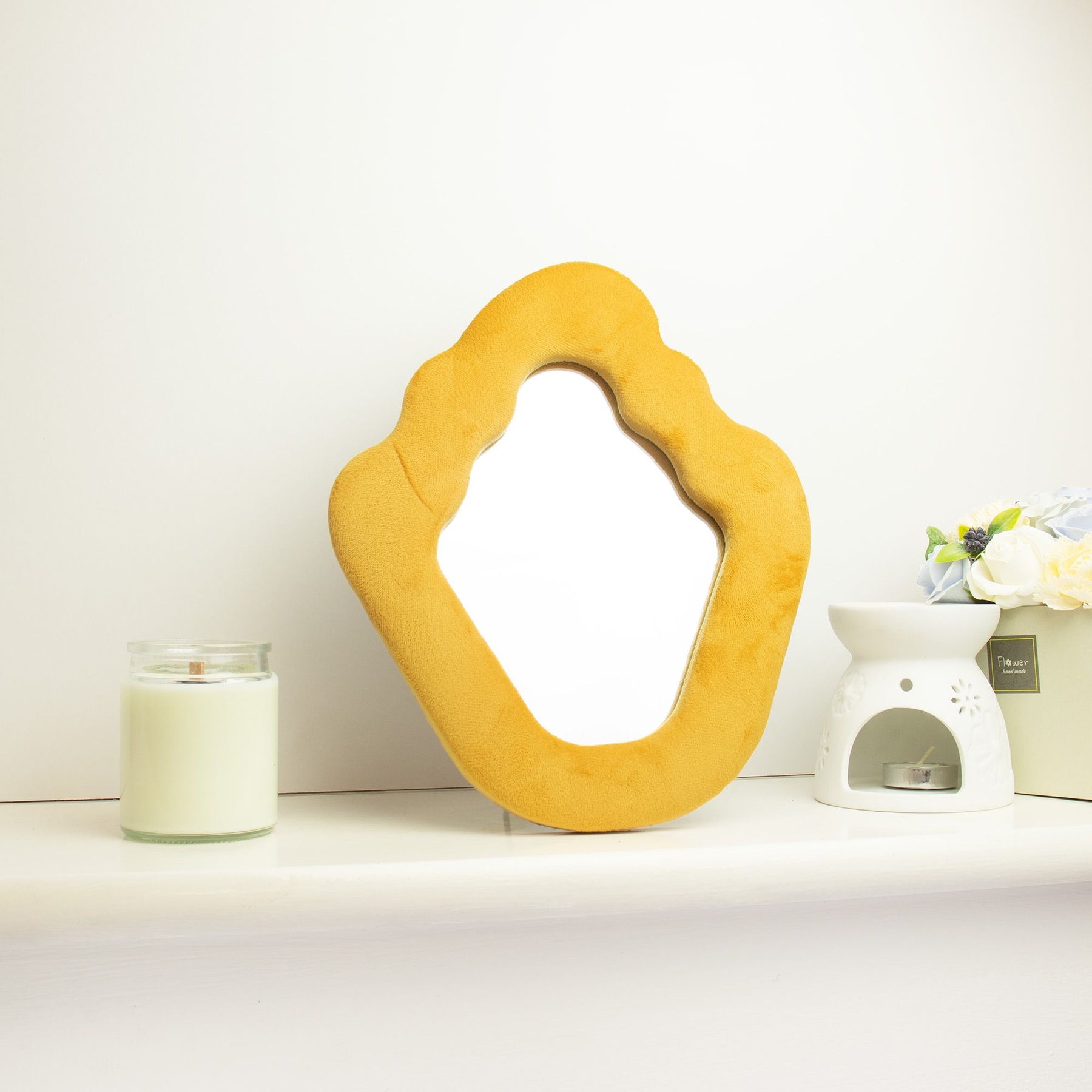 Soft squiggly mirror in vibrant marigold velvet frame with gentle wavy edges, freestanding on white dressing table with soft natural light reflecting in glass