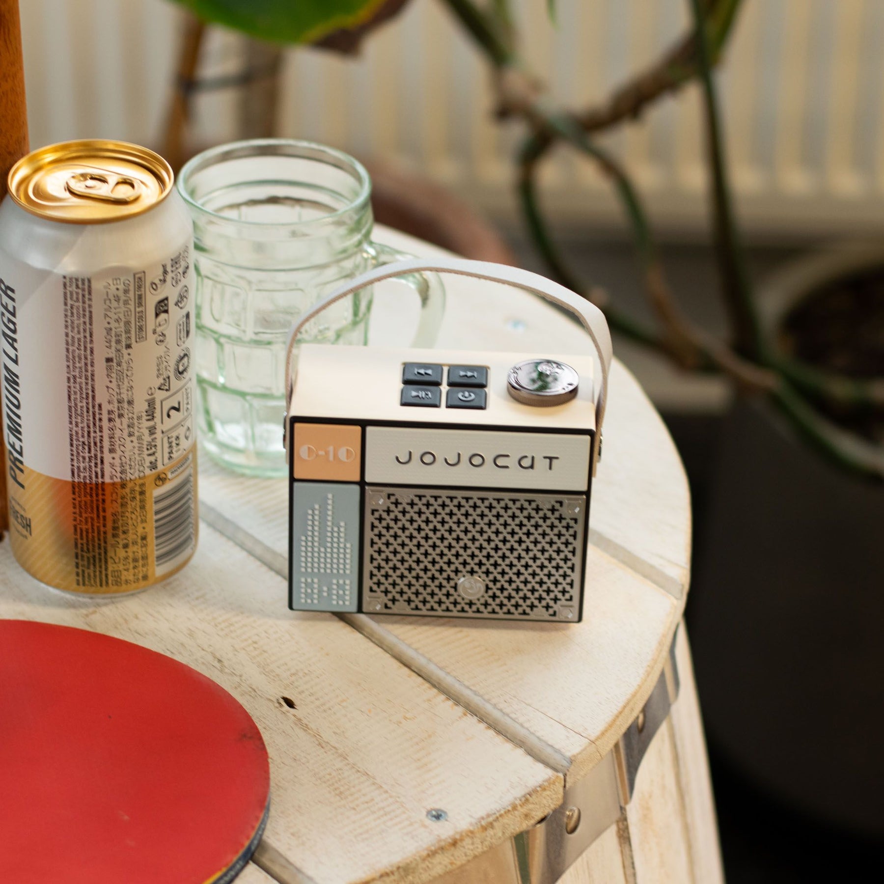 Small radio on a table with a can and a glass jar in the background
