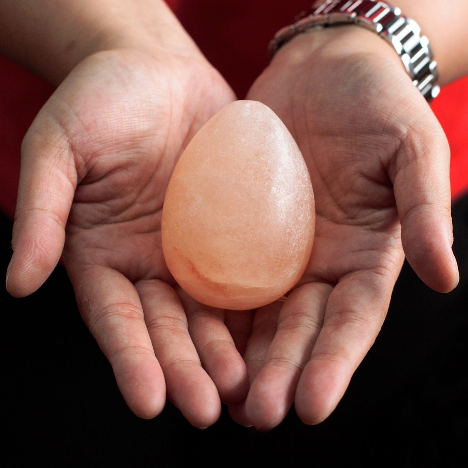 Person holding Himalayan Egg Deodorant Stone between their palms against a black background
