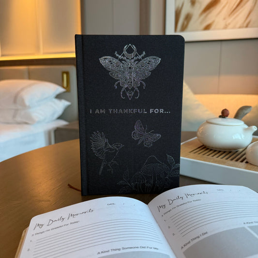 Black notebook with butterfly design on a table with an open book in the foreground.