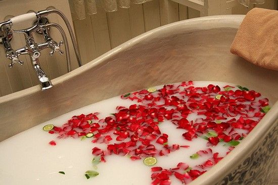 Bath tub filled with bubbles and red soap rose petals, with a towel and faucet in the background.