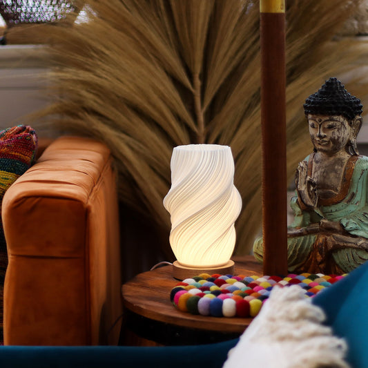Decorative Cloud Twisted New Wave USB lamp with textured honeycomb surface and soft cloud-inspired twisted shape, warm glow on 3rd brightness setting, placed on wooden base on a table with a Buddha statue and colorful balls in a cozy room setting.