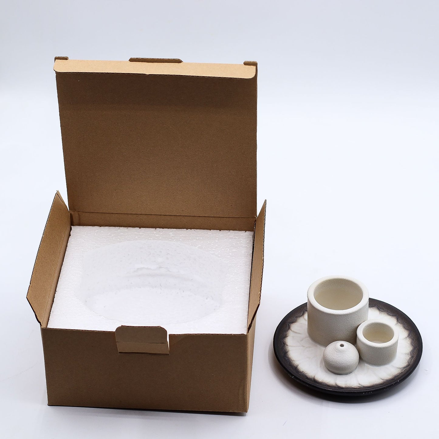Open cardboard box with bubble wrap next to a set of ceramic items on a black plate.