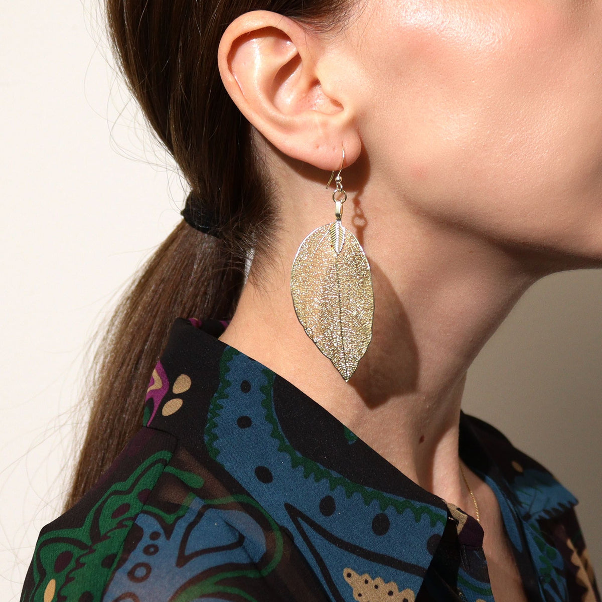 Close-up of a person wearing a silver leaf-shaped earring