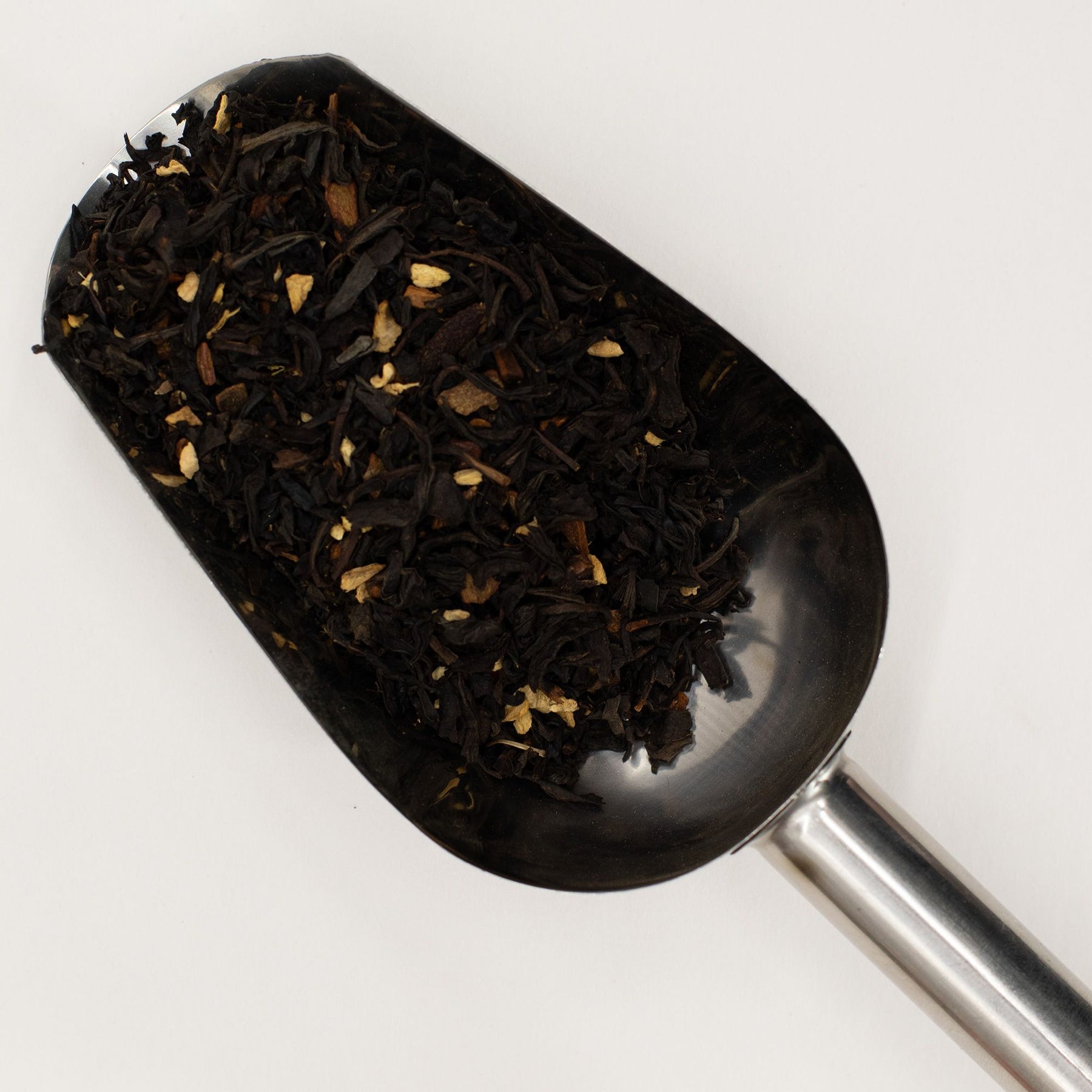 Spoon filled with black tea leaves on a white background