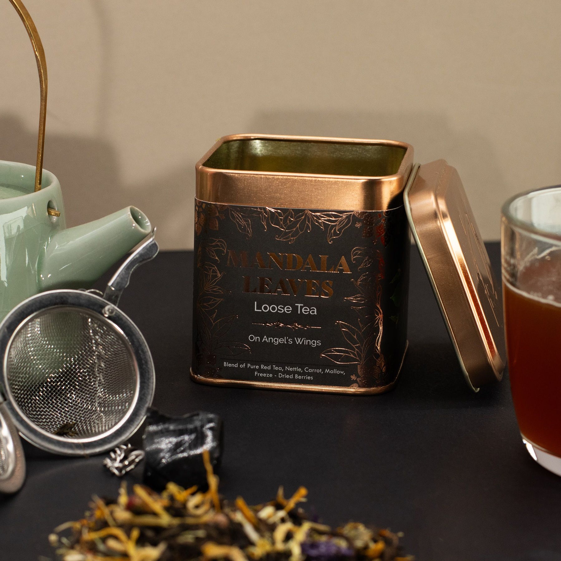 Tea canister with loose tea leaves, teapot, and glass on a dark surface