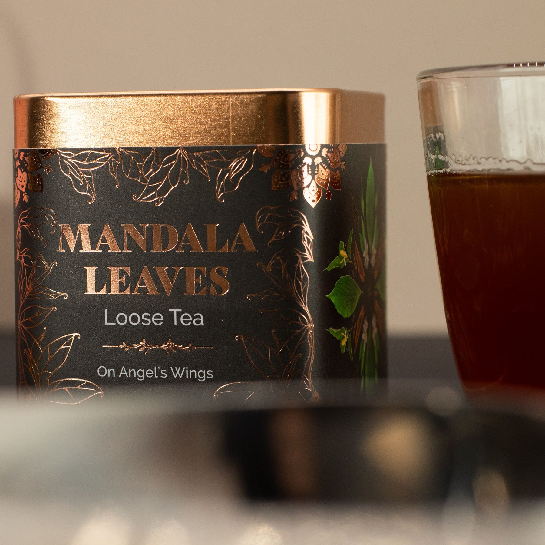 Mandala Leaves loose tea canister with a glass of tea on a neutral background