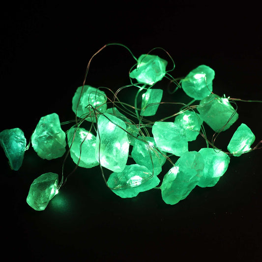 Crystal jade fairy lights glowing soft green in glass bowl on wooden desk with bamboo, coins and prosperity crystals in calming setting