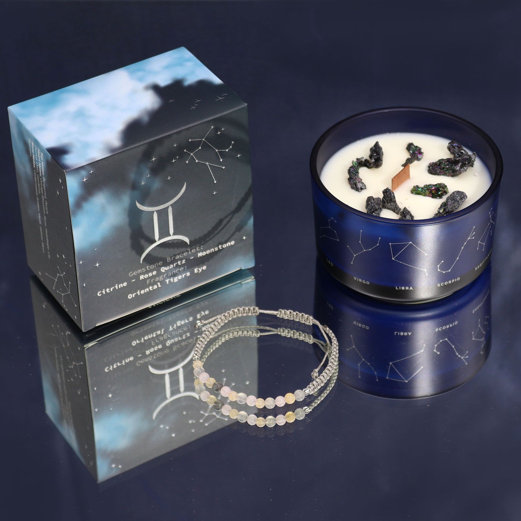 Candle with gemstones, packaging, and bracelets on a reflective surface
