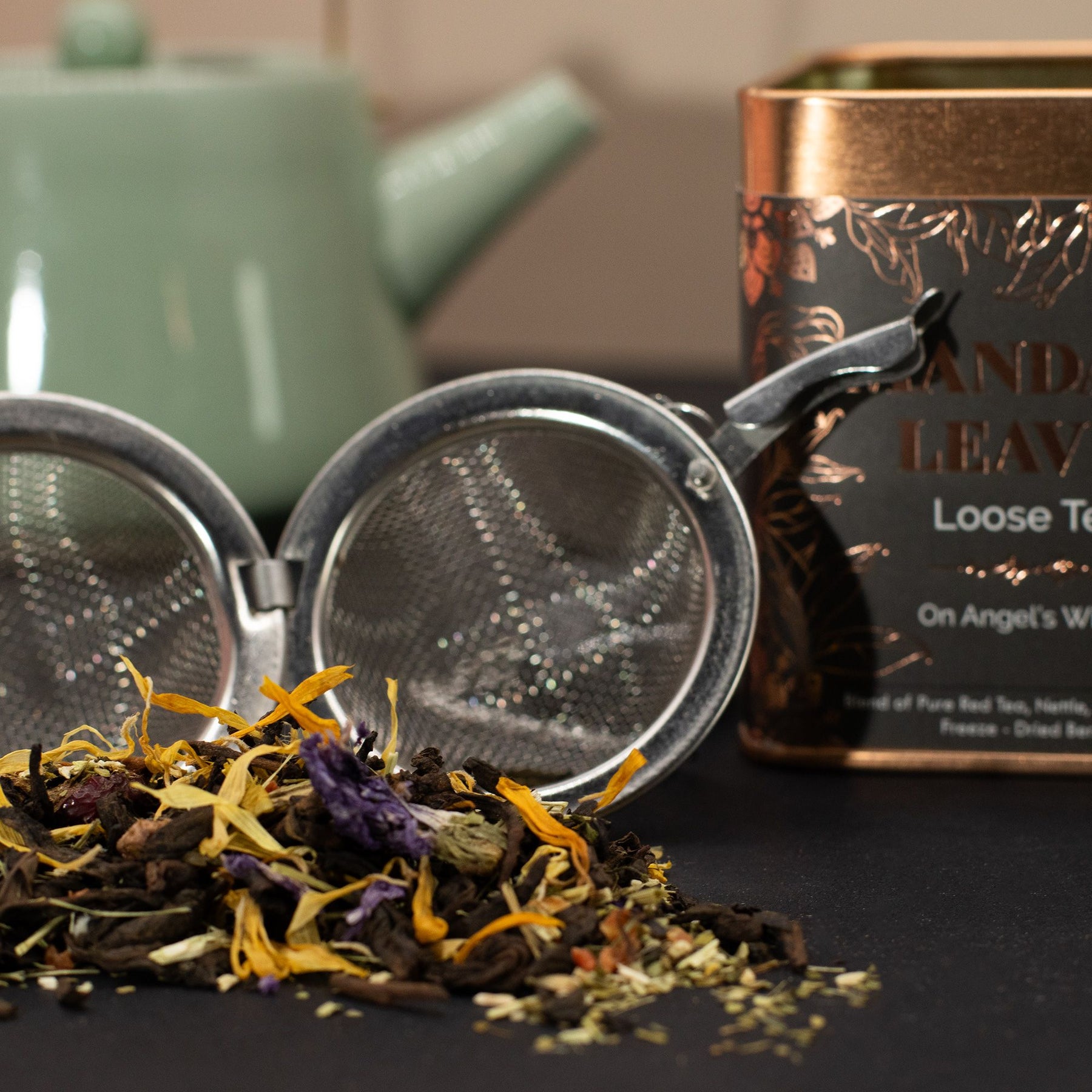 Tea leaves, tea strainer, and tea packaging on a dark surface