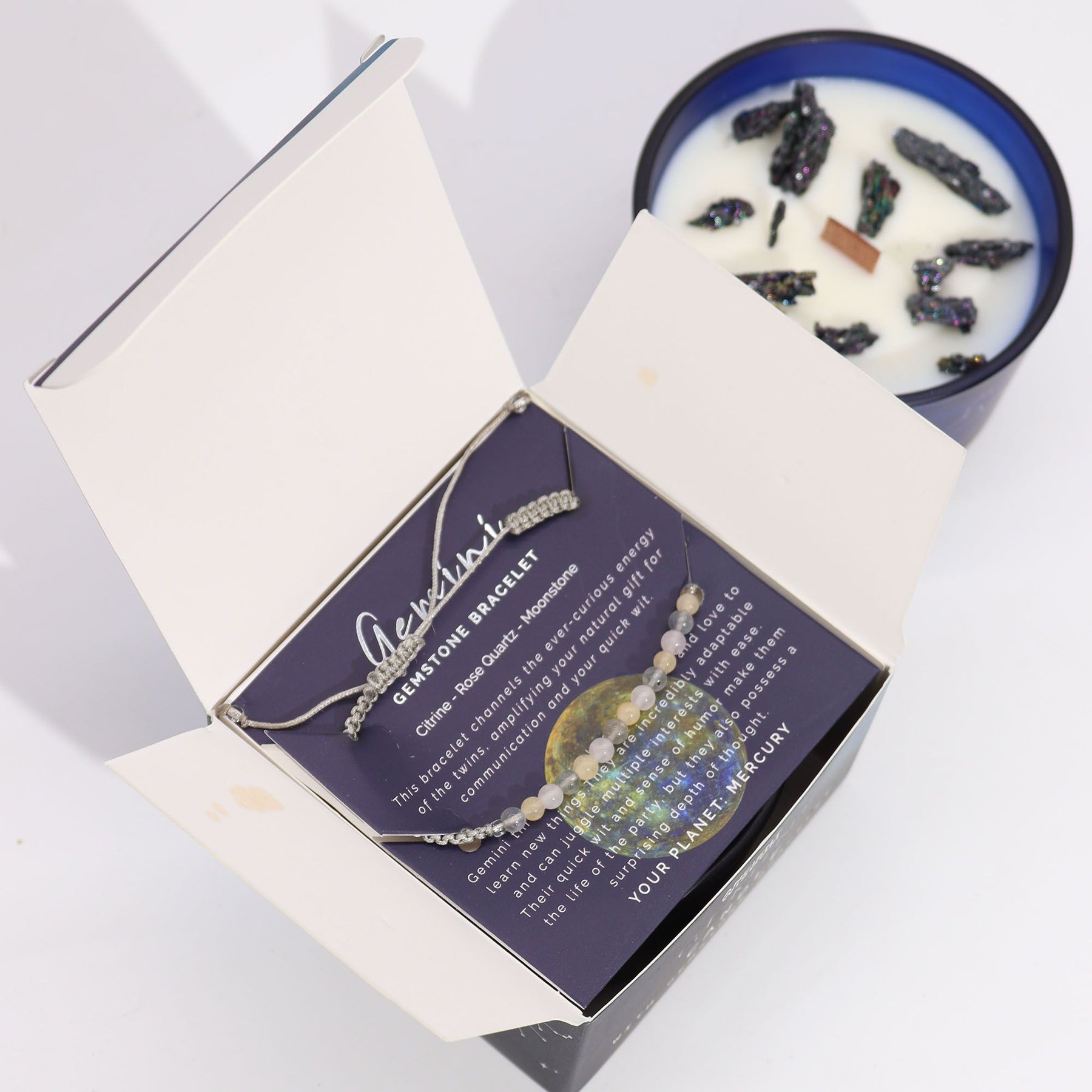 Jewelry set with necklace and bracelet on a card, next to a candle in a box.