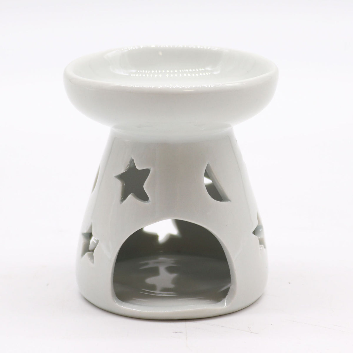 Classic white ceramic oil burner with moon and star cut-out design glowing with tealight on cosy winter evening table