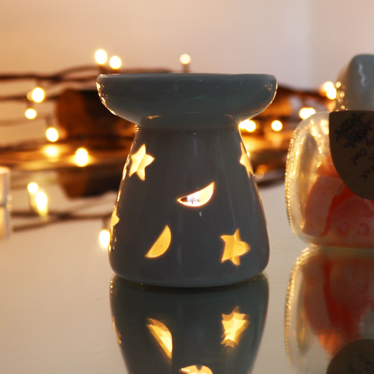 Classic white ceramic oil burner with moon and star cut-out design glowing with tealight on cosy winter evening table